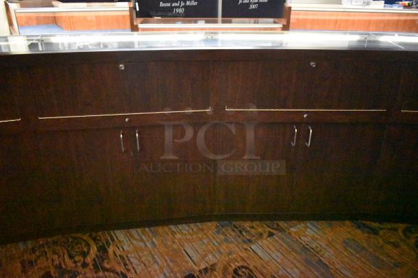 Curved wooden jewelry display case with lighting, four rear doors, in used condition. Buyer must remove item.