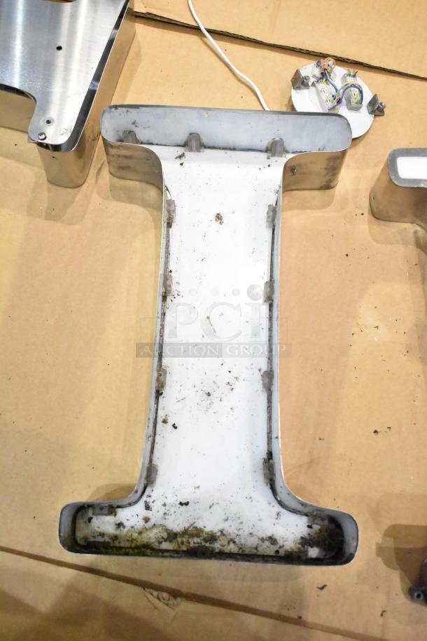 White "I" letter with silver finish frame, showing signs of wear and dirt. Frame has a partially visible wiring component.