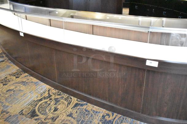 Curved wooden jewelry case with glass top, three rear doors, and three drawers. Lighted interior. Buyer removes.