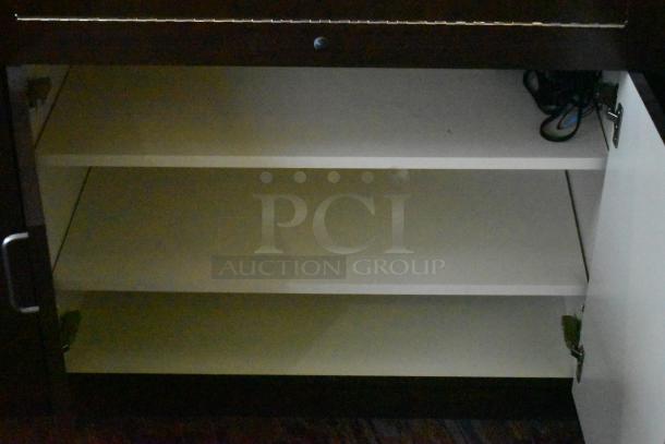 Wooden lighted jewelry case with three rear doors and three drawers, shown with open shelves. Buyer removal required.