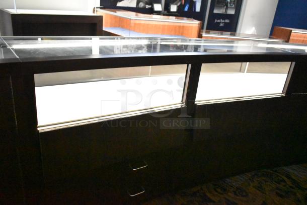 Wooden lighted jewelry display case with three rear doors and three drawers, featuring a glass top. Buyer must handle removal.