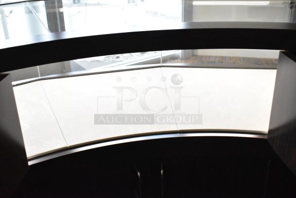 Wooden curved jewelry case with lighting, glass top, and four rear doors. Bring tools for removal. Good condition.