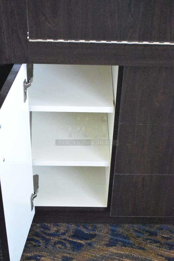 Wooden lighted jewelry case with 3 rear doors, 3 drawers, open shelving, dark wood finish. Buyer must remove.