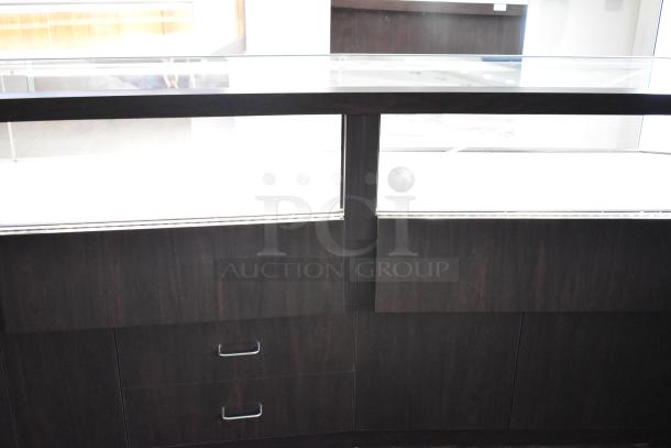 Wooden lighted jewelry case with glass top, 3 rear doors, and 3 drawers. Buyer removal required; bring tools and manpower.