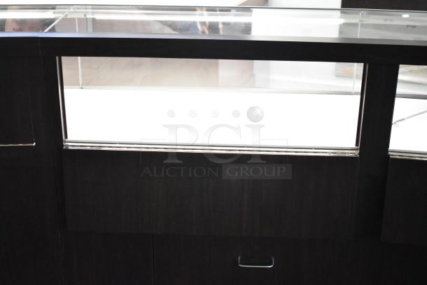 Wooden lighted jewelry case with three rear doors and three drawers. Dark finish, must bring tools to remove.