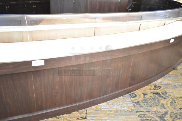 Wooden lighted jewelry case with curved glass front, four rear doors, and dark wood finish. Bring tools for removal.