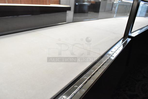 Wooden lighted jewelry case with four rear doors, beige interior, glass top, and metal trim. Buyer removal required.