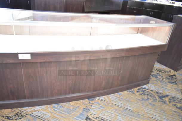 Wooden lighted jewelry case with glass top, 3 rear doors, and 3 drawers. Dark wood finish. Some assembly required for removal.