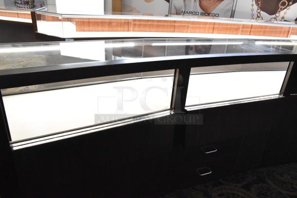 Wooden lighted jewelry case with glass top, three rear doors, and three drawers. Buyer must remove, bring tools.