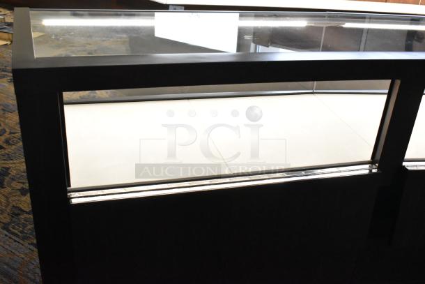 Wooden lighted jewelry case with glass top, three rear doors, and three drawers. Buyer must bring tools to remove.