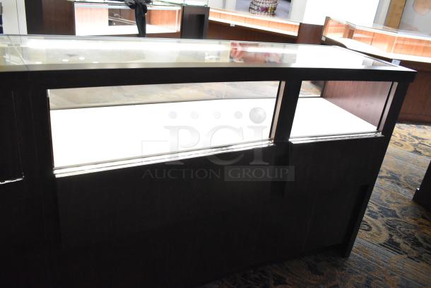 Wooden lighted jewelry case with glass top, 4 rear doors, good condition. Buyer must bring tools and manpower for removal.