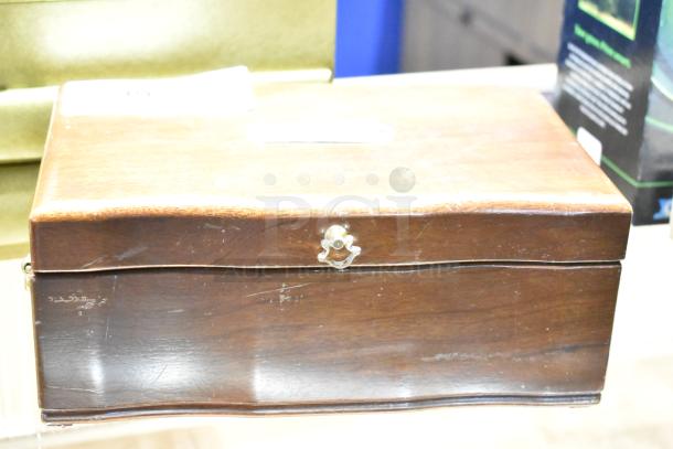 Wooden jewelry case with contents including a watch, pin, and necklaces. Slight wear on surface. Secure clasp closure.