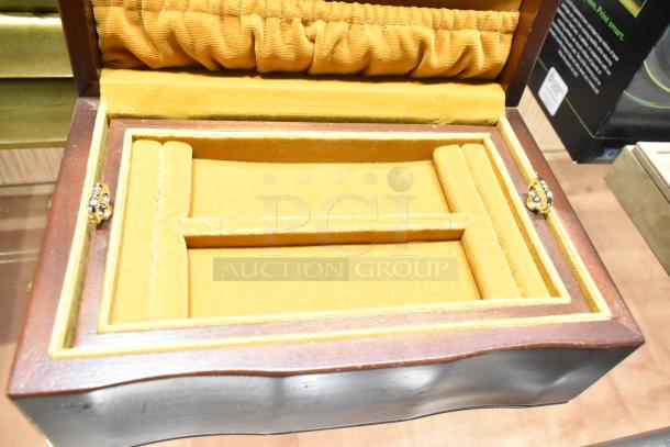 Open jewelry case with yellow velvet lining, empty interior, wood exterior, and ornate gold-toned clasps.