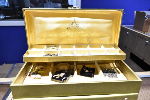 Two gold jewelry cases with dividers, containing a watch, pin, and necklaces. Intricate design on lid. Mixed jewelry items included.
