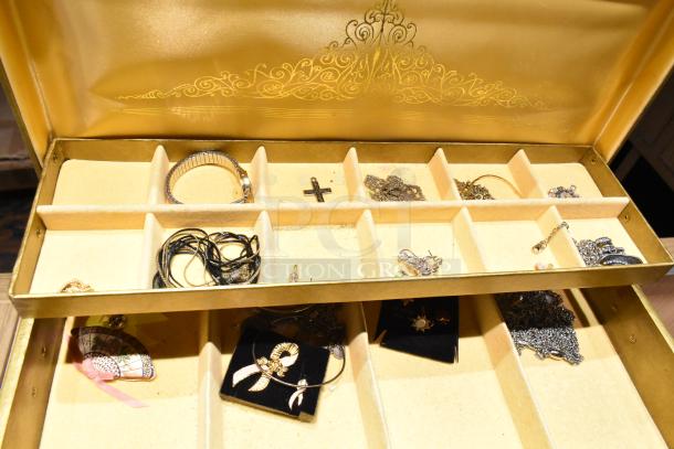 Gold jewelry case with multiple compartments containing a watch, cross pin, necklaces, and assorted jewelry pieces.