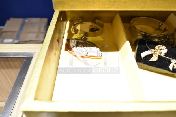 Two jewelry cases with contents include a watch, decorative pin, and necklaces. Cases show mixed jewelry inside.