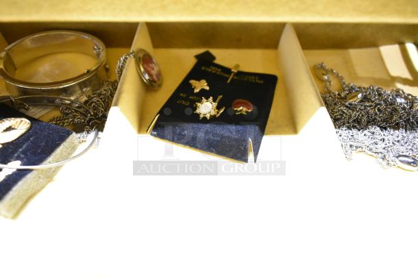 Two jewelry cases containing a watch, a decorative pin, and silver necklaces; visible contents include a gold and pearl pin, heart-shaped item on card.