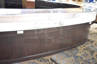 Wooden lighted jewelry case with curved glass top, three rear doors, and three drawers. Must bring tools for removal.