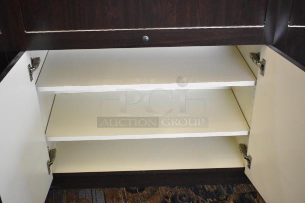 Wooden lighted jewelry case with 3 rear doors and drawers. Features shelves for storage. Buyer must bring tools for removal.