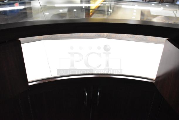 Wooden curved lighted jewelry case, features glass top and four rear doors. Requires buyer removal. Bring tools.