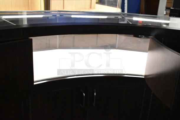 Wooden curved lighted jewelry case with four rear doors. Dark wood finish, modern design. Buyer must dismantle.