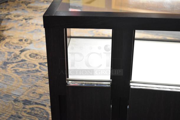 Wooden lighted jewelry case with 4 rear doors and 3 drawers. Dark wood finish, glass top. Buyer must remove.