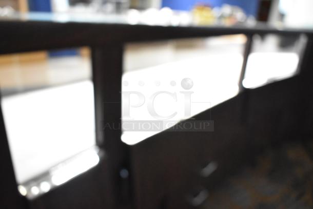 Blurred image of a wooden lighted jewelry case with four rear doors and three drawers, requiring tools and manpower for removal.