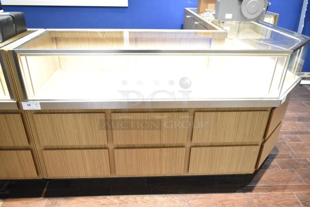 Wooden lighted jewelry case with glass top, four rear drawers, no key. Requires tools and manpower for removal.