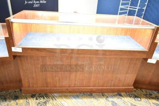 Wooden lighted jewelry case with two rear doors, three drawers, and glass top. Requires tools and manpower for removal.