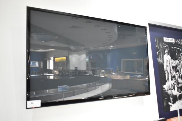 Samsung Television mounted on a wall, large screen, glossy finish, in-store setting. Buyer must remove.