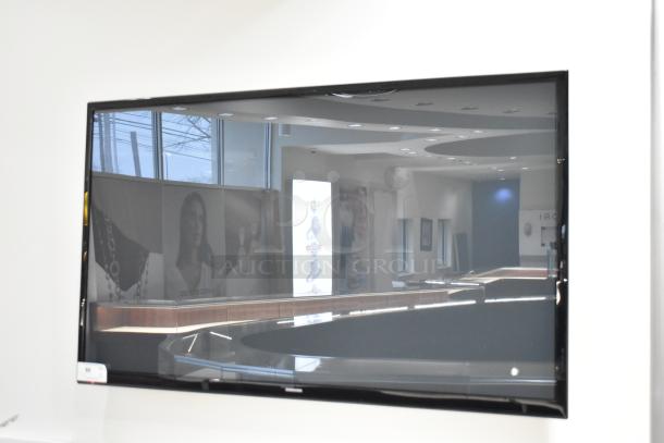 Samsung television, wall-mounted, reflective screen, modern design, condition appears good. Buyer must bring tools for removal.