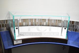 Curved glass countertop display case with metal supports, in excellent condition, features key lock and wooden base.