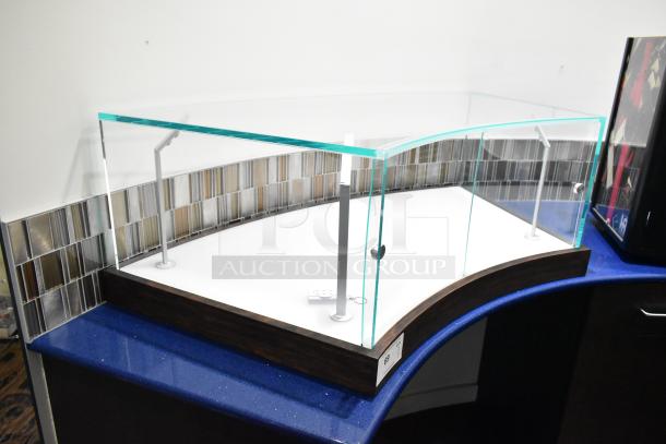 Sleek glass countertop display case with curved wood base, metal supports, and small attached remote. Ideal for showcasing items.