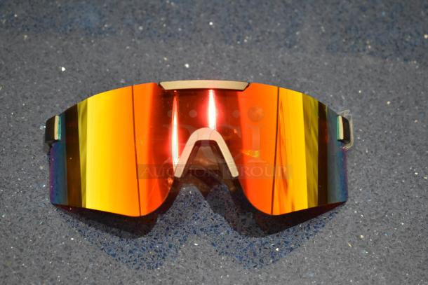 Brand new golden framed sunglasses with sleek orange lenses and a modern design on a blue textured background.