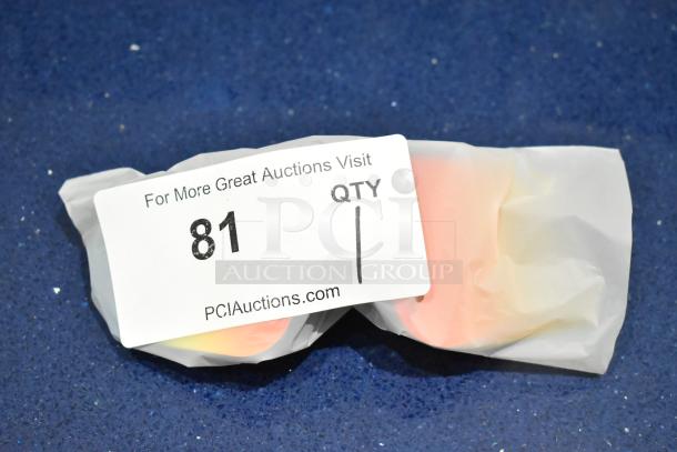 Brand new tan framed sunglasses with orange lenses, wrapped in paper. Auction tag reads "81" from PCIAuctions.com.