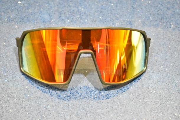Brand new tan framed sunglasses with orange reflective lenses laid on a textured surface.