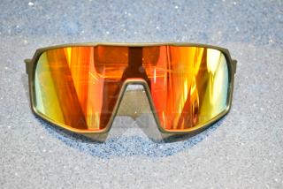 Brand new tan framed sunglasses with orange reflective lenses laid on a textured surface.