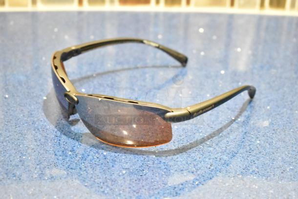 Brand new gray framed sunglasses with BluBlocker brown lenses, displayed on a blue surface.