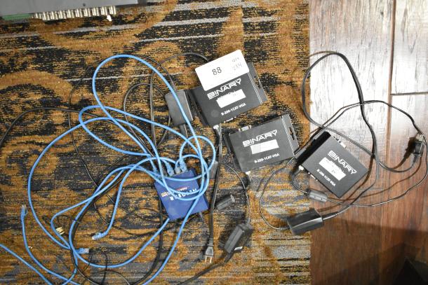 Four items: 3 Binary B-200-1CAT-VGA transmitters with labels and 1 Netgear GS105 ProSafe 5 Port Gigabit Switch with cables.