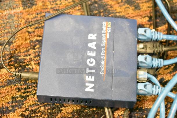 Netgear GS105 ProSafe 5 Port Gigabit Switch with connected wires on patterned carpet. Visible branding and ports.