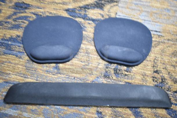 Black ergonomic mouse pads with wrist support on patterned surface.