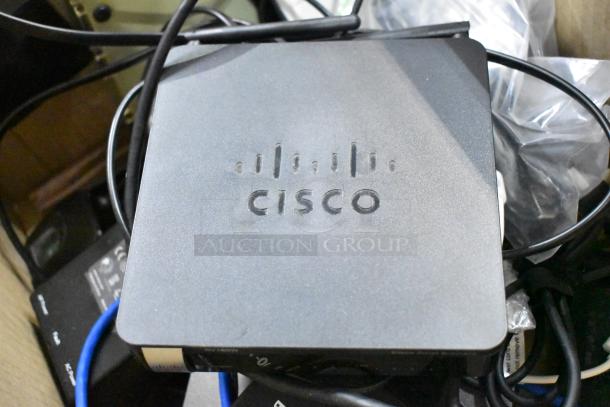 Cisco RV180W Multifunction VPN Router on a pile of electronics, cables visible. Suitable for network enhancement.