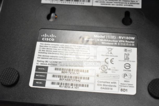 Cisco RV180W Multifunction VPN Router, featuring compliance labels, model number, and serial details visible on the device.