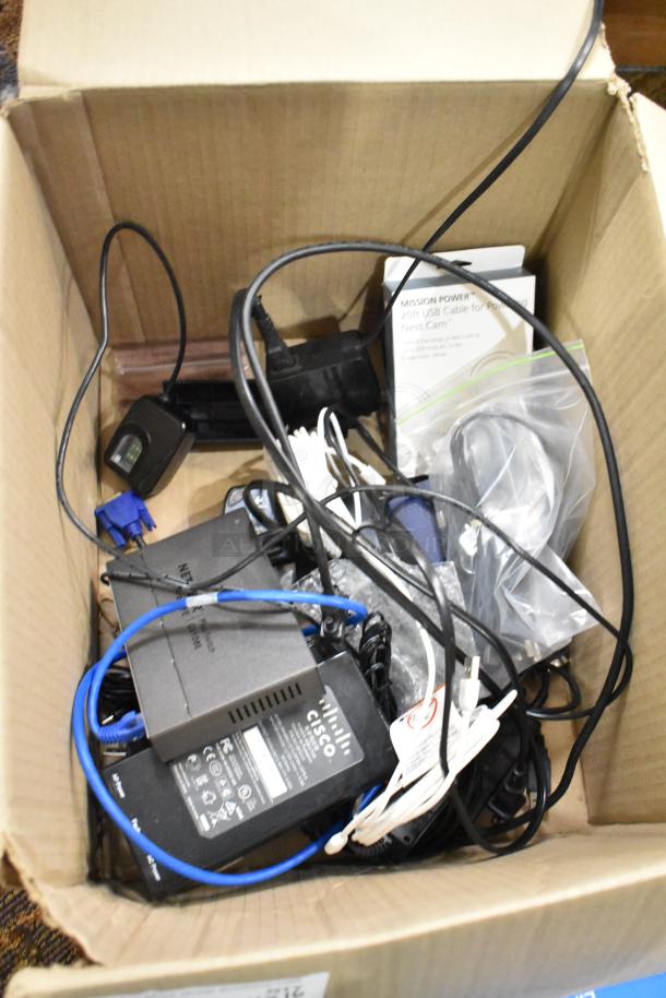 Box of 16 items: Insignia phone cord, HDMI cable, mouse pads, Binary B-200-1CAT-VGA, Cisco RV180W router, Netgear switch.