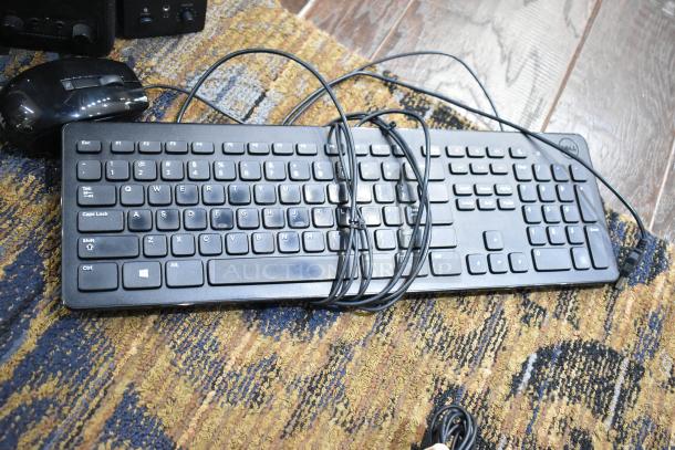 "Various items including black Dell keyboard, mouse, and Logitech speakers on a patterned rug; cables visible."