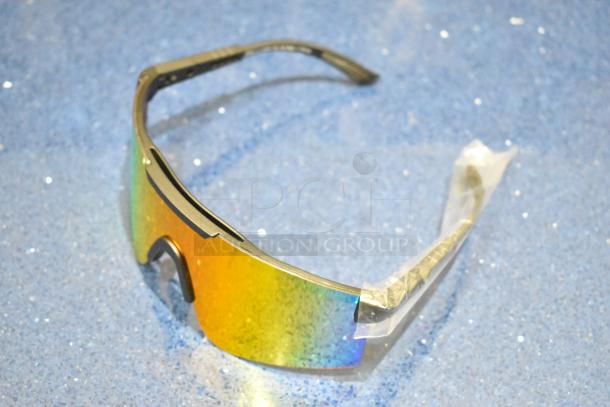 Brand new golden framed sunglasses with orange lenses, wrapped in protective plastic, displayed on blue surface.