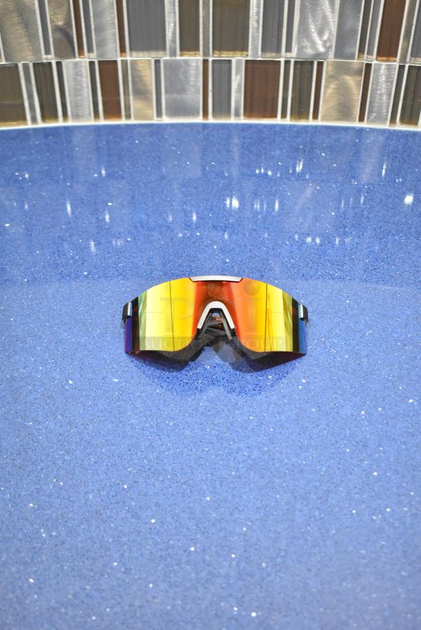 BRAND NEW gray framed sunglasses with reflective BluBlocker orange lenses on blue surface.
