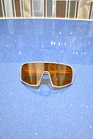 Brand new white-framed sunglasses with BluBlocker brown lens, modern design on a blue surface.