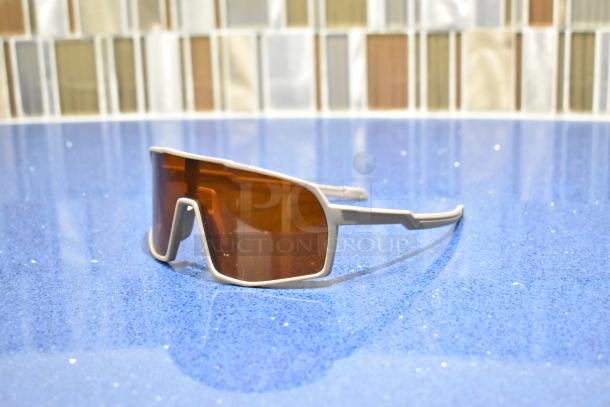 Brand new white framed sunglasses with BluBlocker brown lenses on a blue speckled surface.