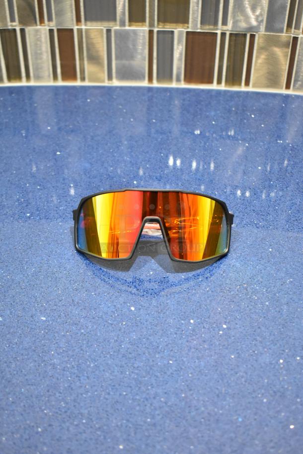 Brand new gray framed sunglasses with BluBlocker orange lenses on a blue surface.